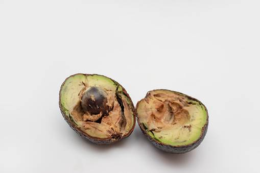 two halves of cut rotten avocado on a white background