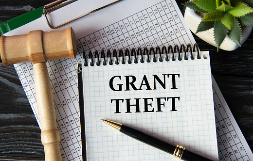 GRANT THEFT - words on a white sheet on the background of a judge's gavel, a cactus and a pen