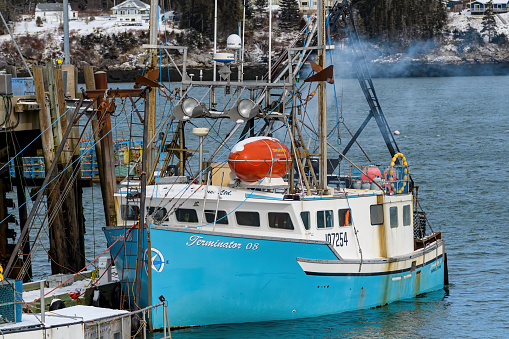 Dipper Harbour, NB, Canada - 2024-02-18: A fishing boat docked at low tide. Smoke billows from it as it prepares to sail.