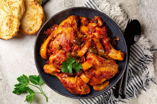 Chicken cacciatore, hunter-style italian chicken with tomatoes,  Taggiasca olives and yellow bell peppers. Bread toast. Directly above.