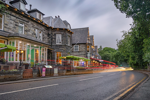 Betws-y-Coed, United Kingdom - June 30, 2023 : Car light trails on a quaint road going through a small village in North Wales