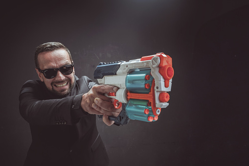 A man with sunglasses is holding a toy gun in his hand, looking serious and ready for action.