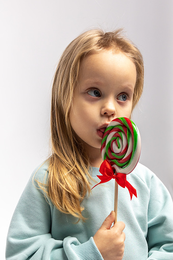 Portrait of funny little blonde girl with sweets lollipop in her hand. High quality photo