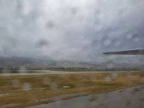 Two commercial airplanes parked on a wet tarmac, set against a backdrop of a cloudy, overcast sky.