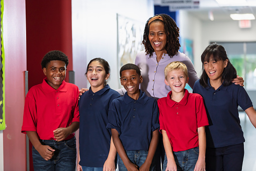An African-American teacher standing with a multiracial group of middle school students in a hallway, smiling at the camera.