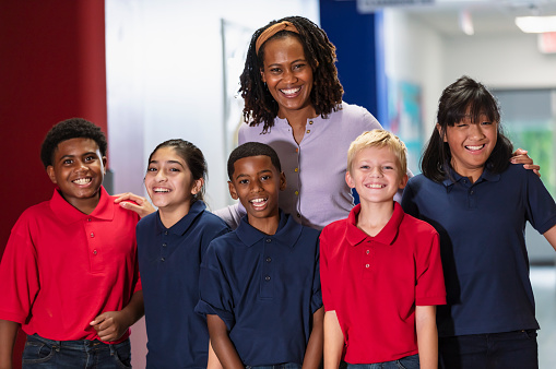 An African-American teacher standing with a multiracial group of middle school students in a hallway, smiling at the camera.