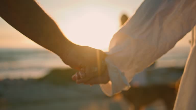 Dating lovers holding hands on sunrise sea beach close up. Couple touching arms