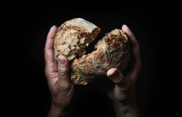 Symbolic gesture of breaking and giving a piece of rustic bread.