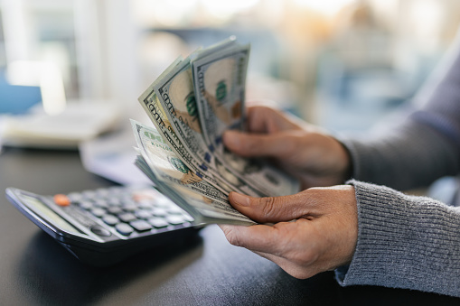 A woman counting a hundred dollar bills. There is a calculator next to her on the table.