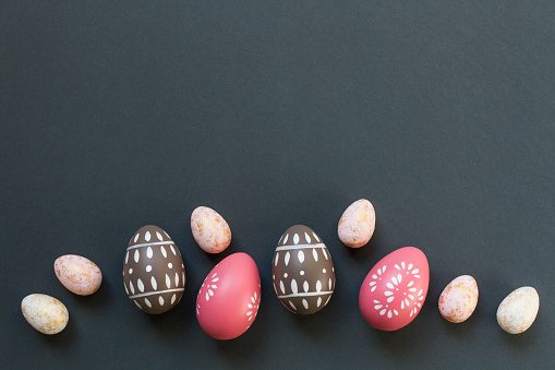 Happy Easter concept with elegant Easter eggs painted in pastel pink and brow colors decorated with spring ornaments on dark gray background with copy space. Elegant Easter banner template. Top view, flat lay. Happy Easter greeting card with space for text. Dots and flowers painted on Easter eggs