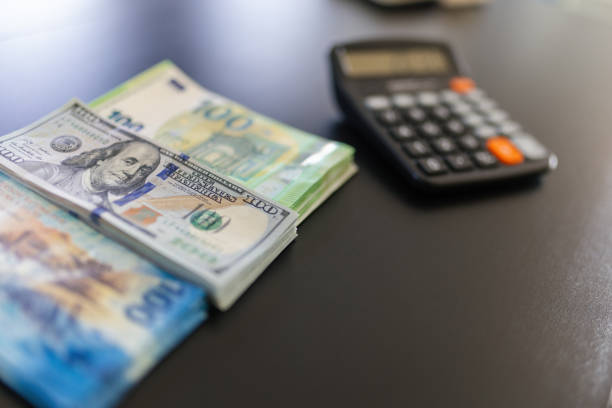 Three piles of different currencies on the table - dollars, swiss and euros, and a calculator.