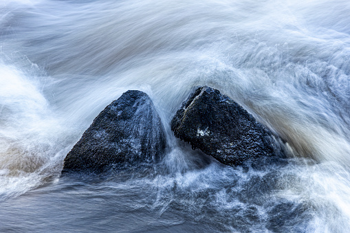 Long exposure of raging river , stone surrounded by churning water