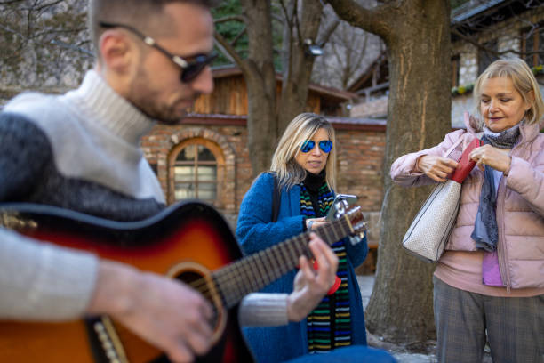 Two senior tourists listening to street musician playing a guitar