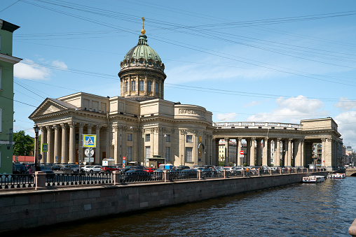 Saint Petersburg, Russia - June 07, 2023: Kazan Cathedral. Cars on the embankment street and water Griboedov canal, old historical center of St. Petersburg, Russia. Clear blue sky