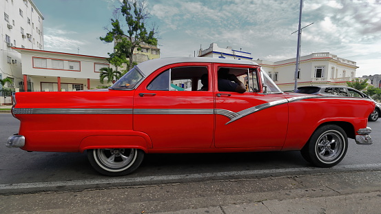 Havana, Cuba-October 07, 2019: Old red American classic car -almendron, yank tank- 1956 Ford Fairlane Town Sedan stopped at a red light on the Linea Street and Avenida Presidentes corner, El Vedado.