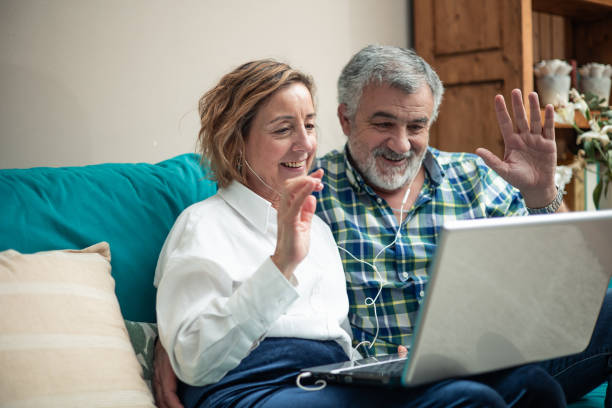 istock elderly couple greeting during video call with laptop on sofa 2023725260