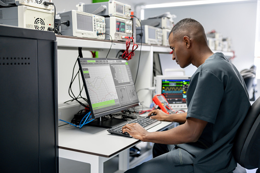 African American technician repairing medical equipment using a multimeter connected to his computer