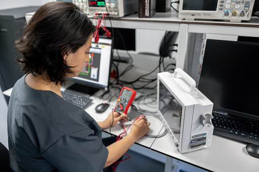 Latin American female maintenance engineer repairing medical equipment using a multimeter