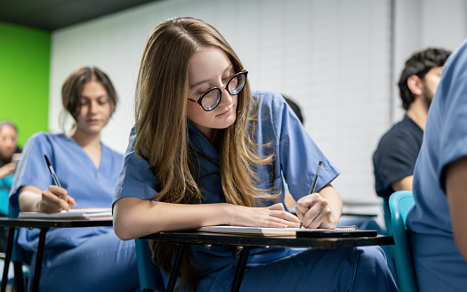 Latin American medical student in class writing notes on her notebook - medical school concepts