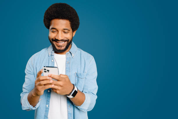 istock Young Latin man with an afro hair beams while using a smartphone 2023756572