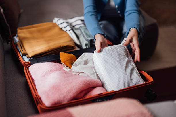 Person Packing Clothes Into an Orange Suitcase for a Trip