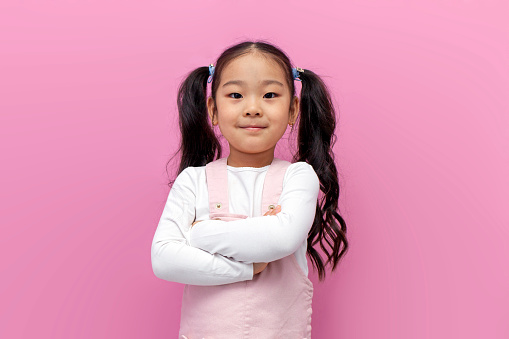 Close up head shot portrait of little brown-haired child girl. Cheerful kid against white studio wall background