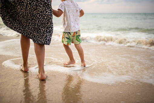 Woman with her little son walking on the beach by the sea in sunset, they are on vacation in Thailand.