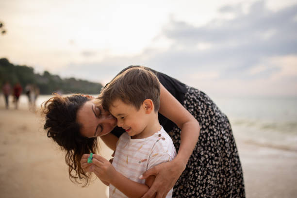 Woman with her little son standing on the beach by the sea in sunset, they are on vacation in Thailand.