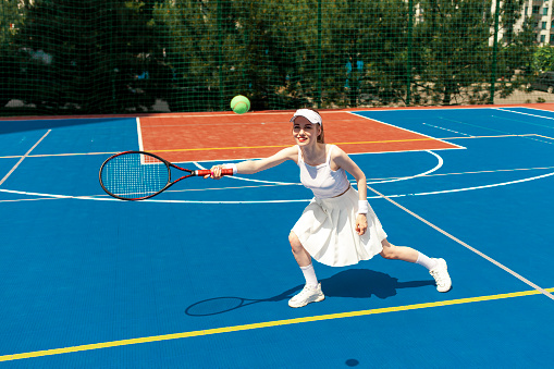 young girl tennis player in white uniform holding racket on tennis court, female athlete playing tennis outdoors