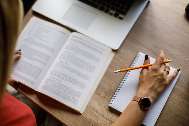Close up shot of unrecognizable young female student studying and writing notes at her desk.