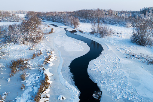 An aerial of a river slowly freezing over on a sunny winter day in rural Estonia, Northern Europe