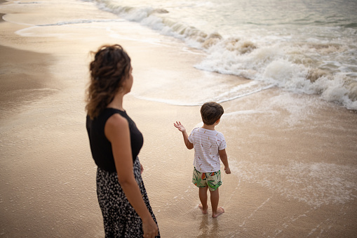 Woman with her little son standing on the beach in sunset, they are on vacation in Thailand.