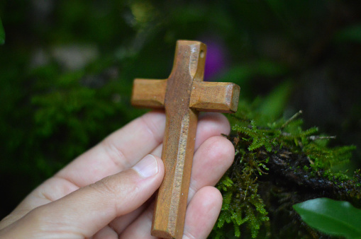 Young woman's hand holding a wooden cross on a natural green background