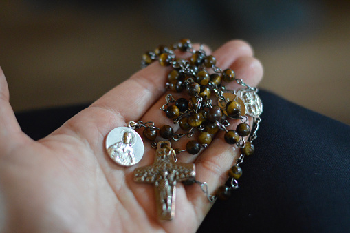 Young woman's hand holding a rosary for prayer with a metal christ