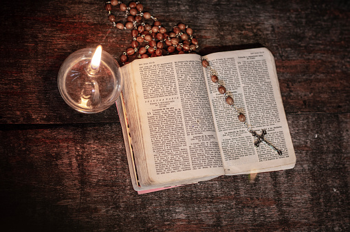 Open Bible with rosary and a lit oil lamp, objects for prayer