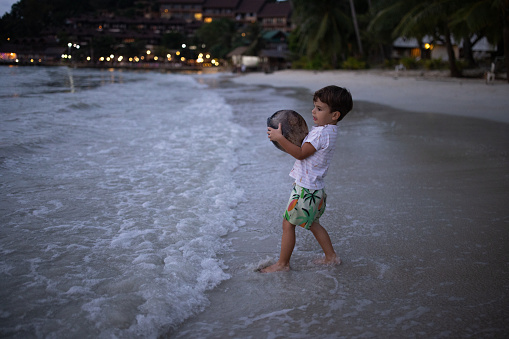 Cute little boy playing with a rock on the beach by the sea in sunset.