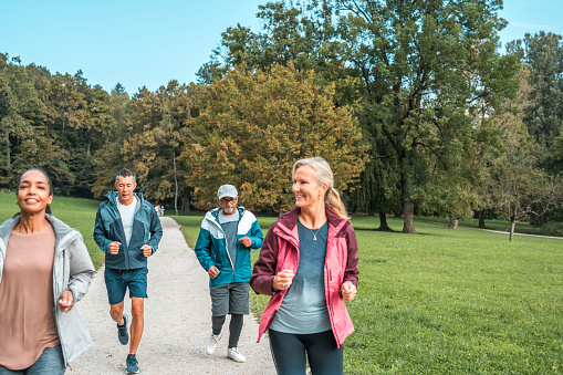 People from different backgrounds embrace a healthy lifestyle by running on a macadam path in a public park, fostering togetherness.