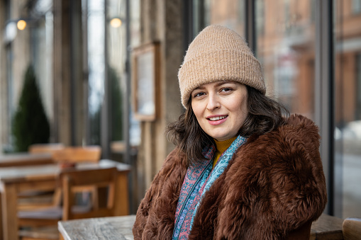 Portrait of a smiling woman in a winter coat and hat in the city, looking at the camera.