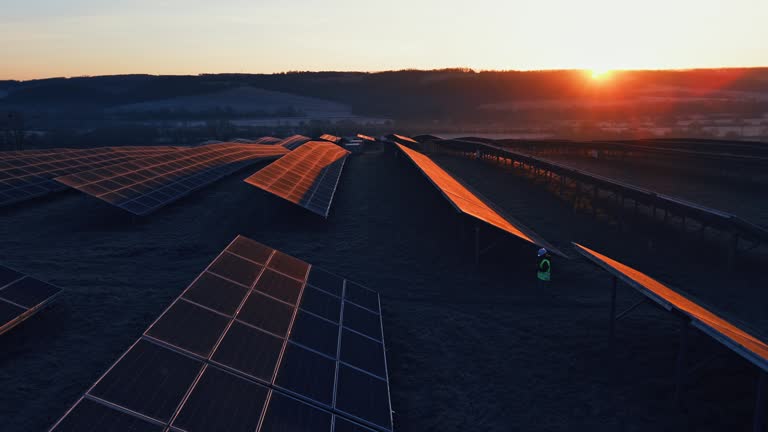 AERIAL Drone Panning Shot of Female Engineer Walking Amidst Solar Panels at Solar Farm During Sunset