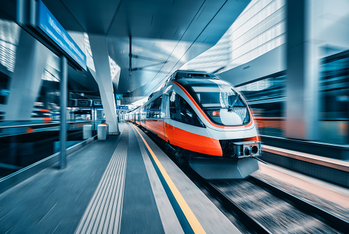 Orange high speed train in motion at modern railway station in Vienna. Fast intercity passenger train with motion blur effect. Railway platform. Railroad in Austria. Commercial transportation. Concept