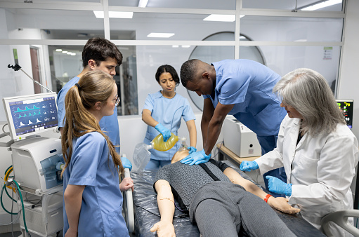 Teacher teaching medical students to perform CPR on a dummy at the hospital - healthcare and medicine concepts