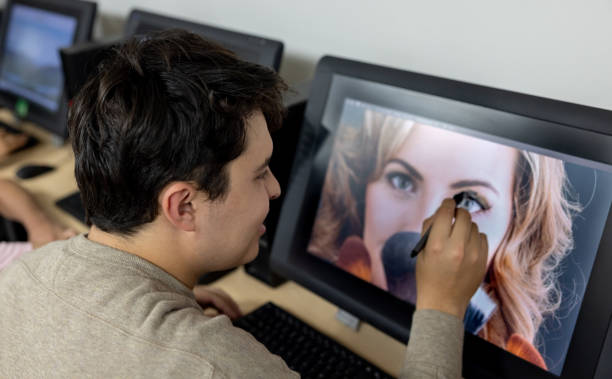 College student retouching a photo in an editing class on his computer using a stylus pen - IT education concepts