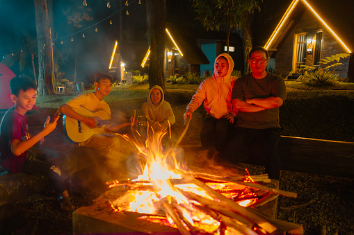 Group of  family having fun playing guitar while camping at the night
