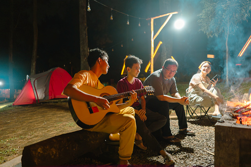 Group of young friends having fun playing guitar while camping.