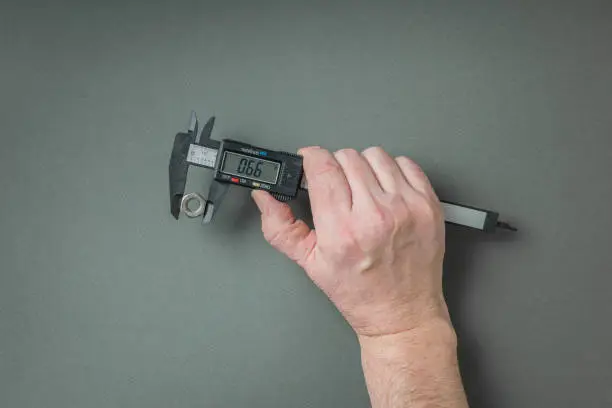 A man's hand with an electronic caliper on a gray background. A tool for accurate measurement of dimensions.