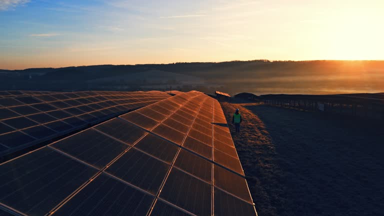 AERIAL Drone Shot of Female Engineer Walking along Large Solar Panels on Farm at Sunset in Slovenia