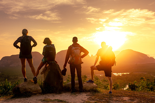 Four young hikers with backpacks and friends are enjoying great view at sea, islands and sunrise. Phang Nga province, Thailand