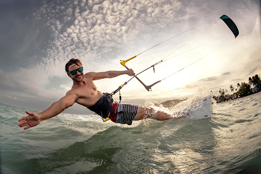 Professional kiter makes the difficult trick on a beautiful background. Kitesurfing Kiteboarding action photos man among waves quickly goes