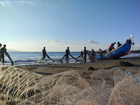 Banda Aceh 09/17/2021 Daily activities of Javanese village fishermen cleaning nets from fish and trash from the catch and putting them back into traditional wooden boats when the beautiful sun sets