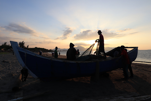 Banda Aceh 12/25/2021  Daily activities of Javanese village fishermen cleaning nets from fish and trash from the catch and putting them back into traditional wooden boats when the beautiful sun sets